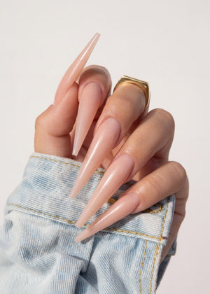 Hand with long, pointed nails wearing a denim jacket on a light background